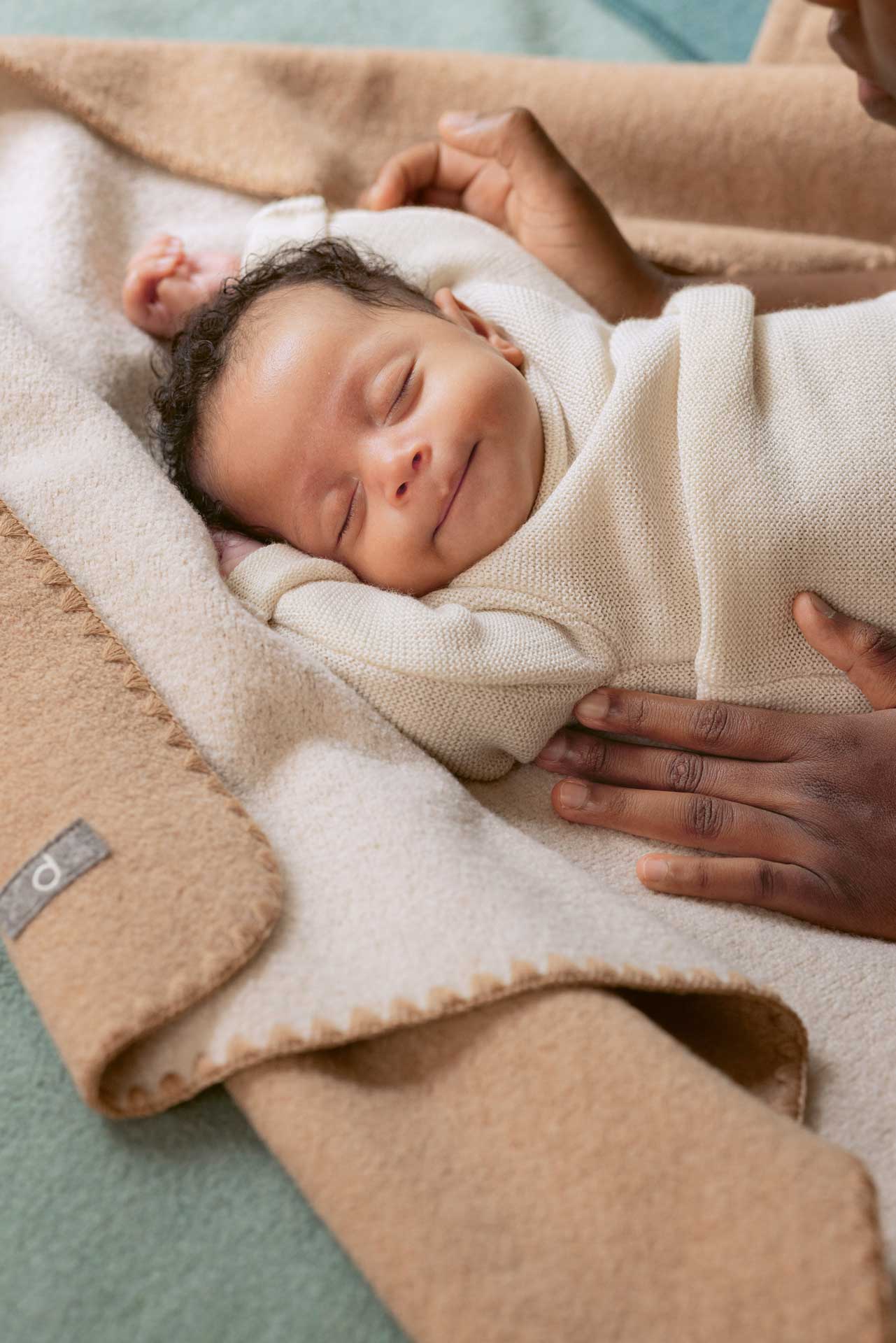 Schlafendes Baby mit naturfarbenem disana Baby-Pullover mit hellbraunem Hautton auf Doubleface-Babydecke in Karamell-Natur