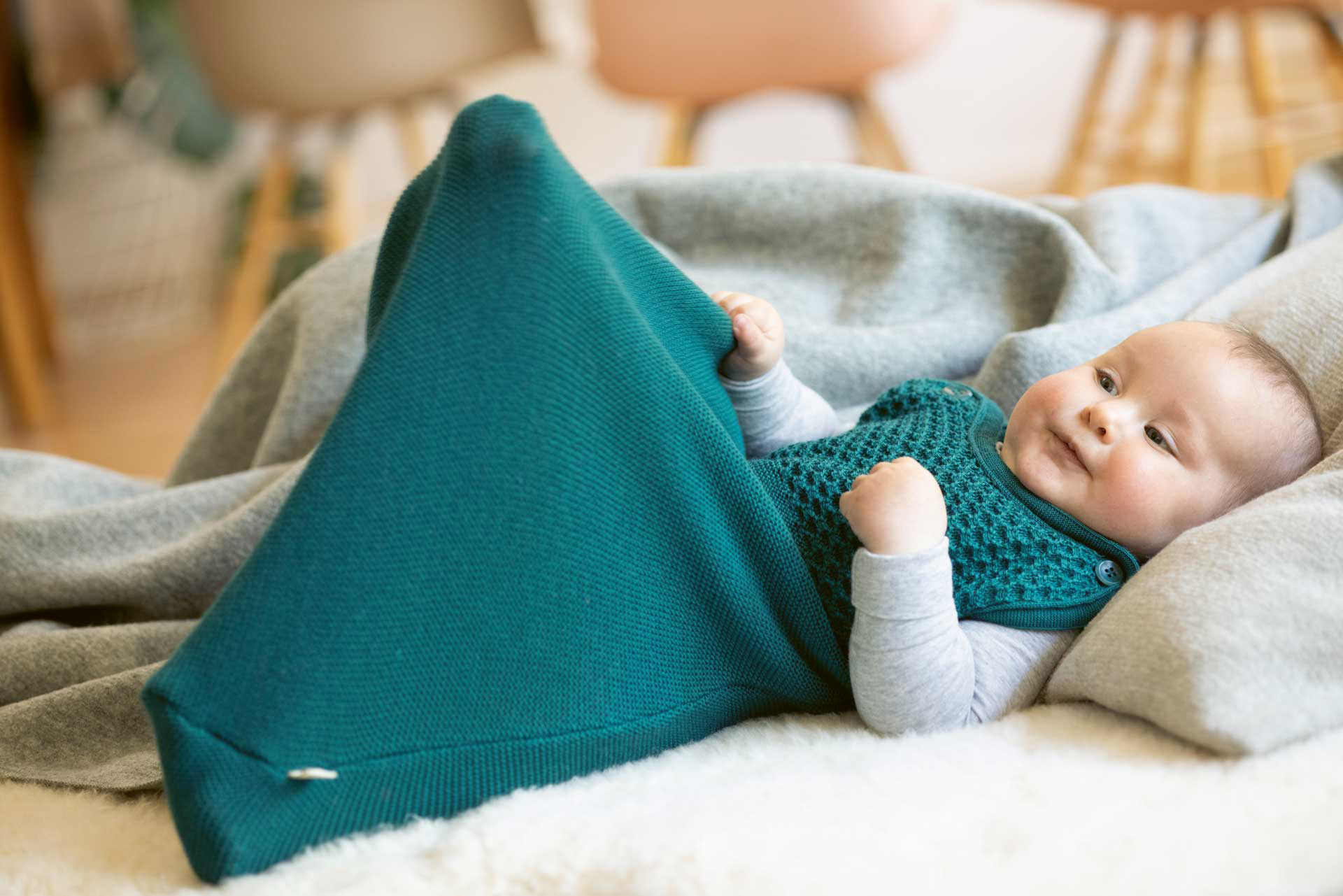 Baby in disana Träger-Schlafsack aus Bio-Merinowolle in der Farbe Pacific auf Lammfell liegend