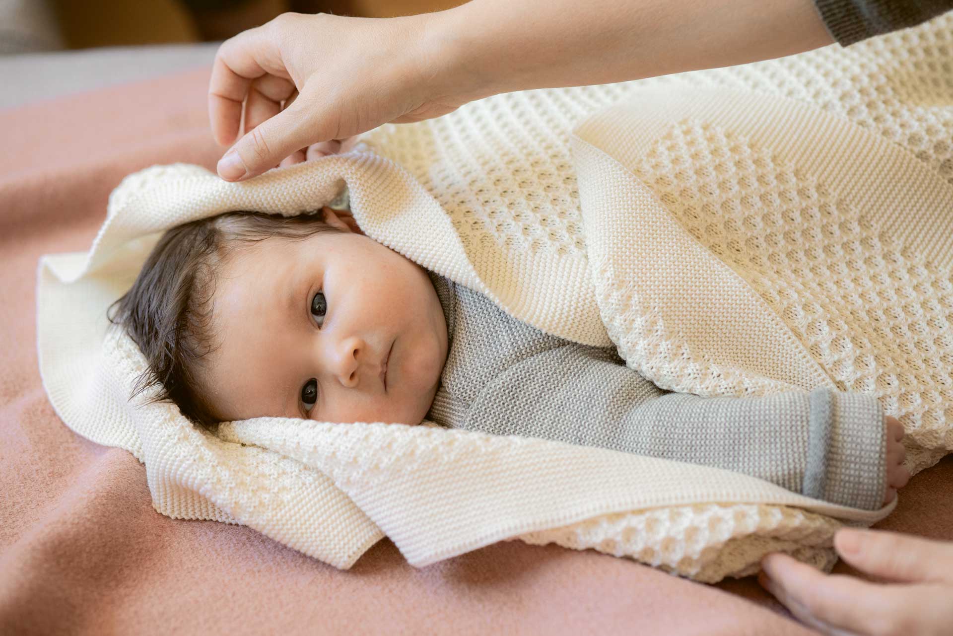 Baby in cremefarbener Strickdecke aus Bio-Merinowolle