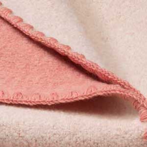 Nahaufnahme der disana Doubleface-Babydecke aus Bio-Merinowolle in Softpink-Natur mit typischer Muschelkante in Softpink