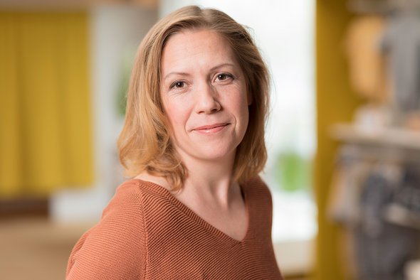 Porträt der disana CEO Aiga Sautter im rostfarbenen Langarm-Shirt, lächelnd im disana Laden in Holzelfingen