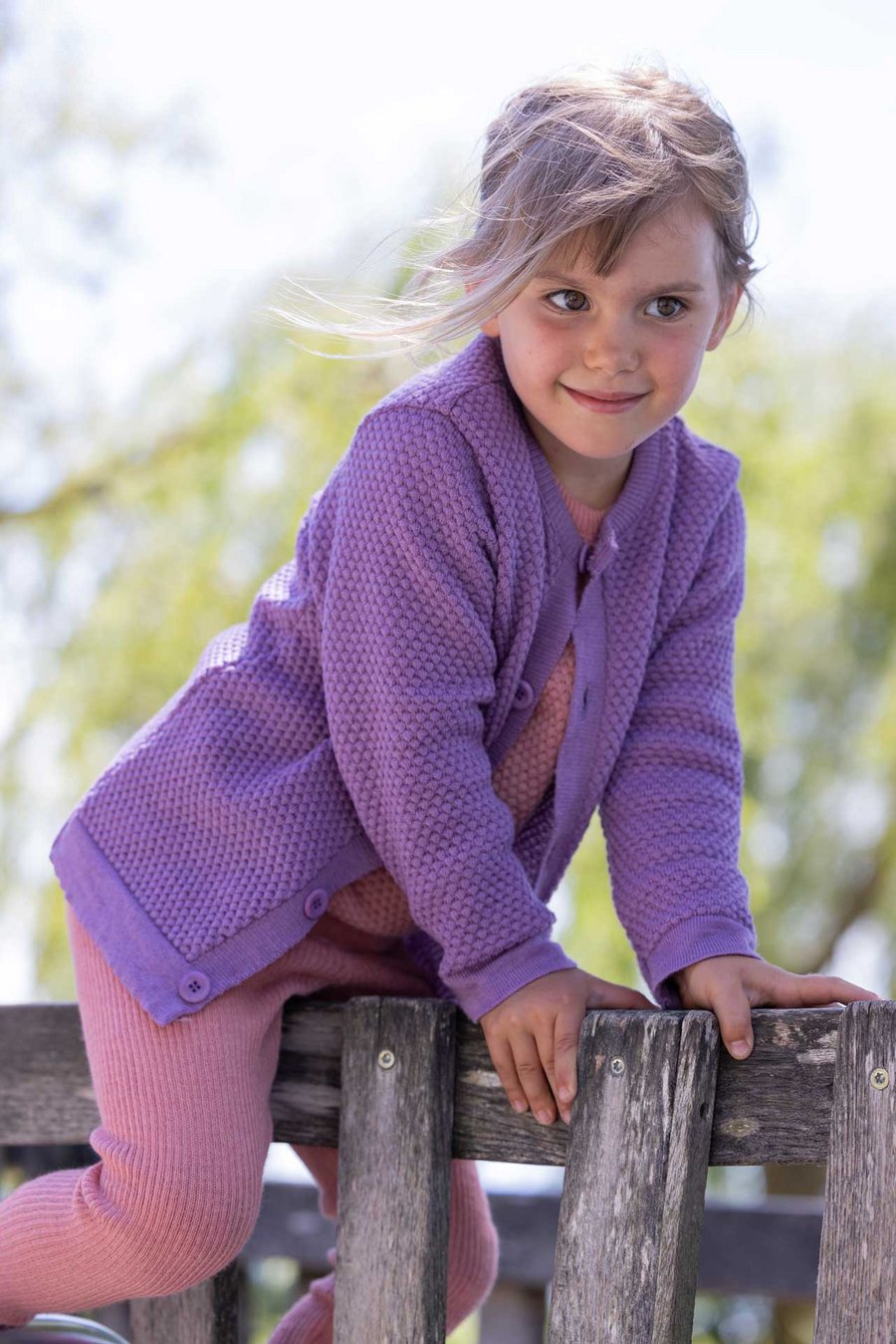 Mädchen trägt disana Waben-Strickjacke Flieder Bio-Merinowolle klettert auf Holzgerüst, Leggings & Wabenstrick-Pulli Softpink