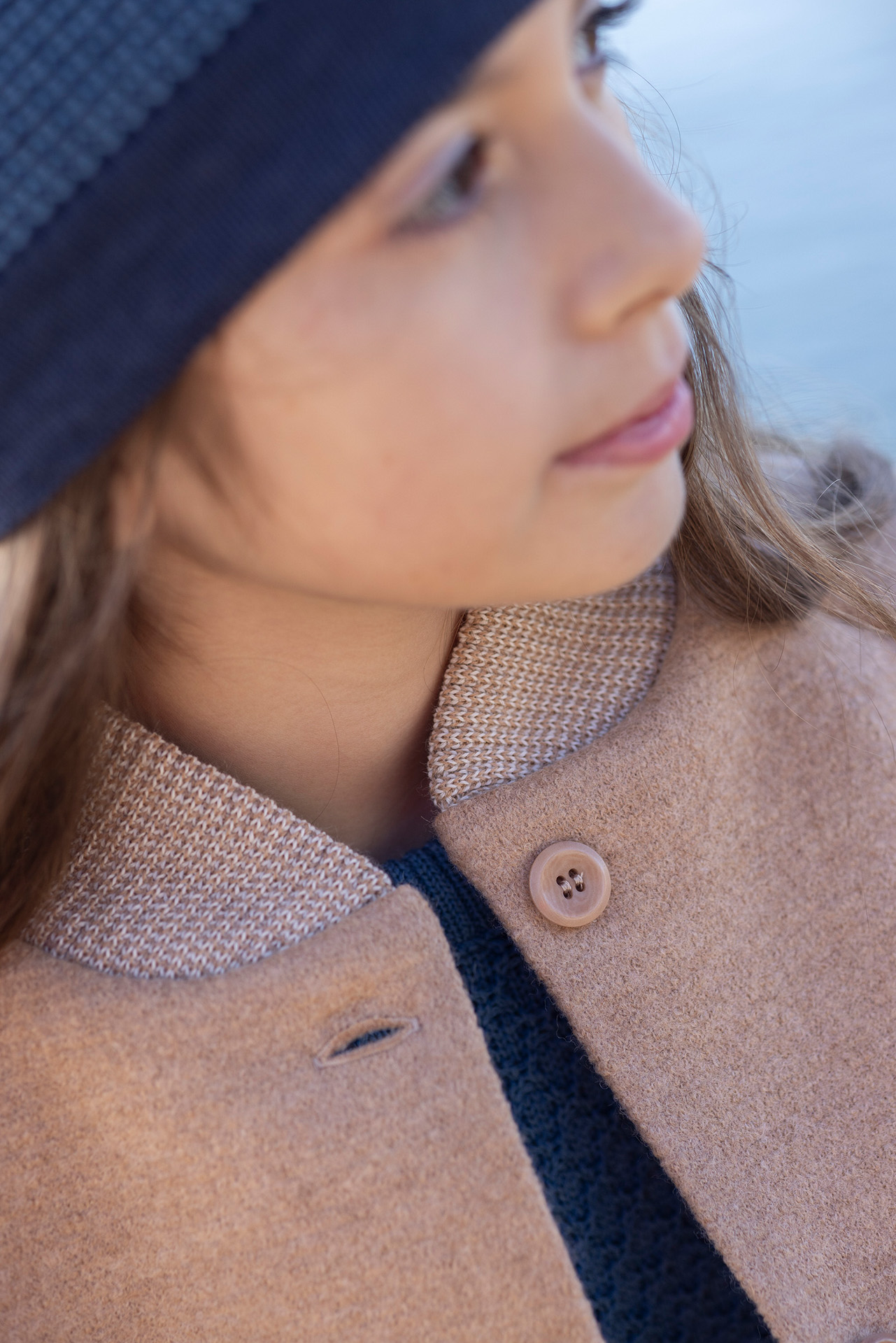 Close Up eines braunhaariges Mädchen im Teenager-Alter mit disana Walk-Mantel Karamell und Beanie in Indigo-Taubenblau