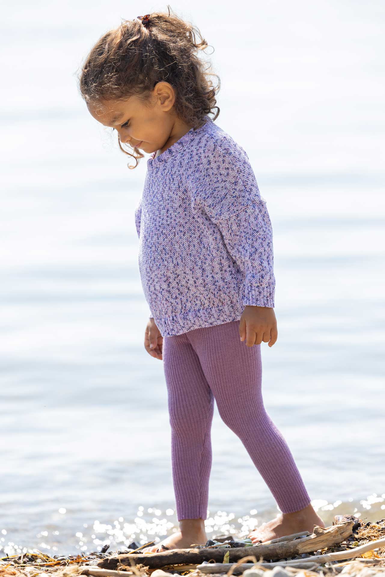 Mädchen mit hellbraunem Hautton in disana Baumwoll-Pullover "Flieder Spray" & Leggings Flieder läuft am Kiesstrand eines Sees