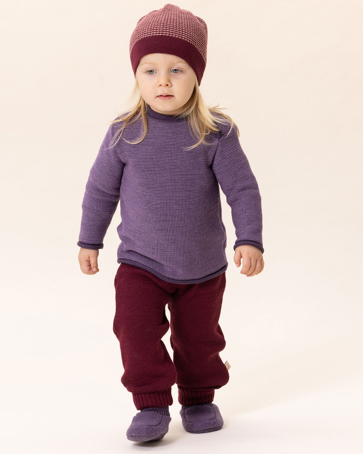Kind in lila Ringelpullover, roter Walkhose und Strickmütze