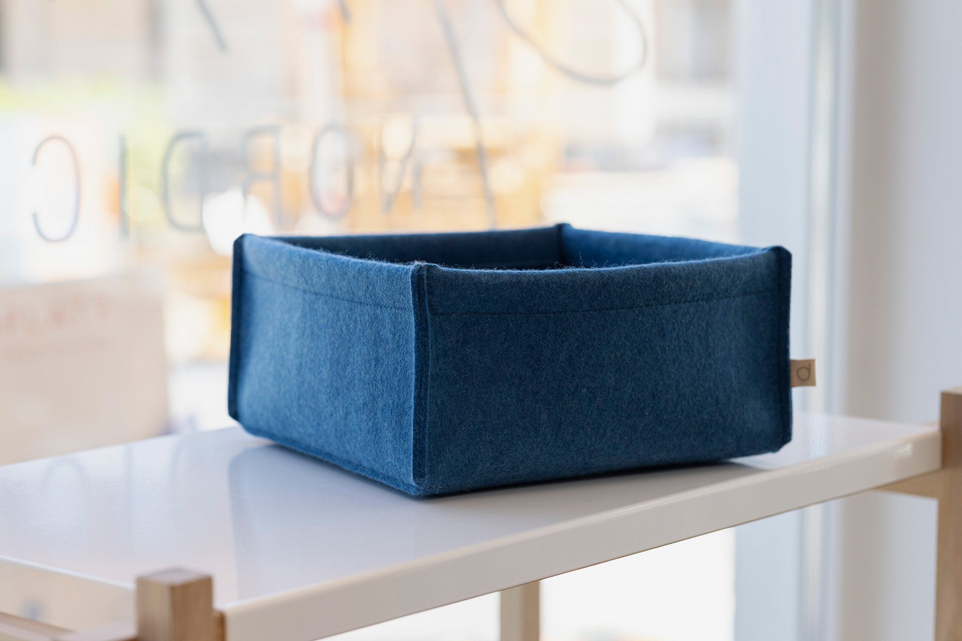 Kleine blaue disana Filz-Box aus Bio-Recycling-Filz auf einem weißen Regal vor einem hellen Fensterhintergrund.