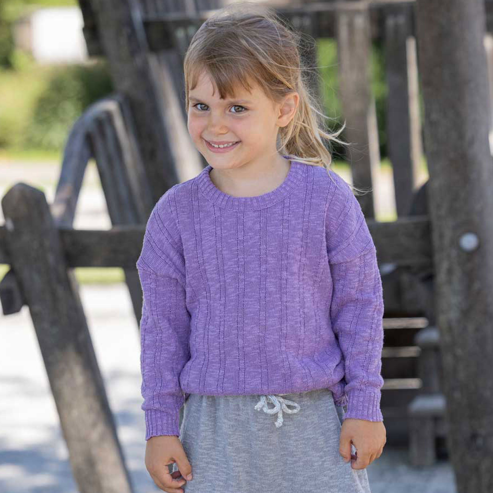 Dunkelblondes Mädchen im lilafarbenen disana Leinen-Pullover aus Bio-Baumwolle und Leinen-Mix auf einem Klettergerüst