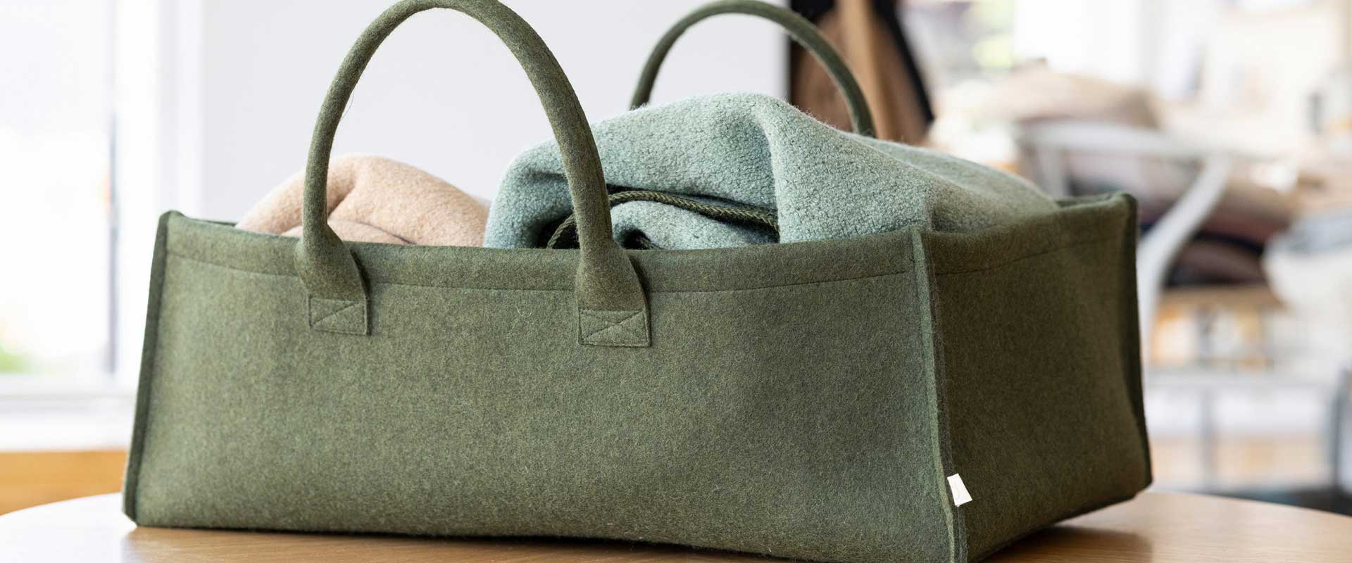 disana Filz Aufbewahrungskorb Oliv, gefüllt mit Doubleface-Decke in Eukalyptus-Jade auf einem Holztisch in einem hellen Raum